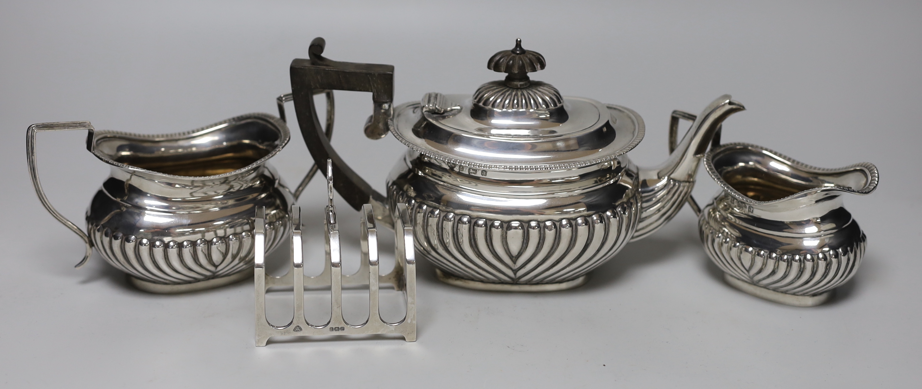 A late Victorian demi-fluted silver three piece tea set, Birmingham, 1899/1900 and a later small silver toastrack, gross weight 24.1oz.
